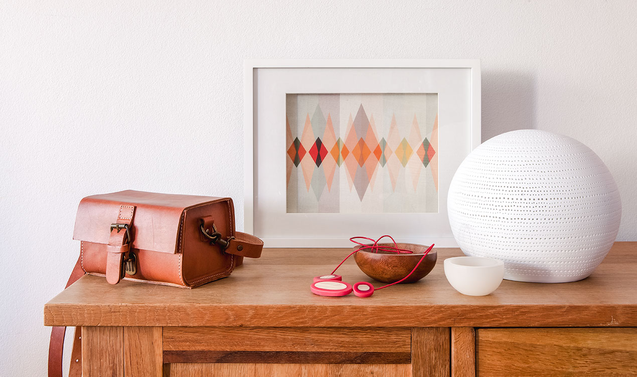 Indie styled product selection with leather bag, framed print, resin necklace, bowls and ceramic lamp.